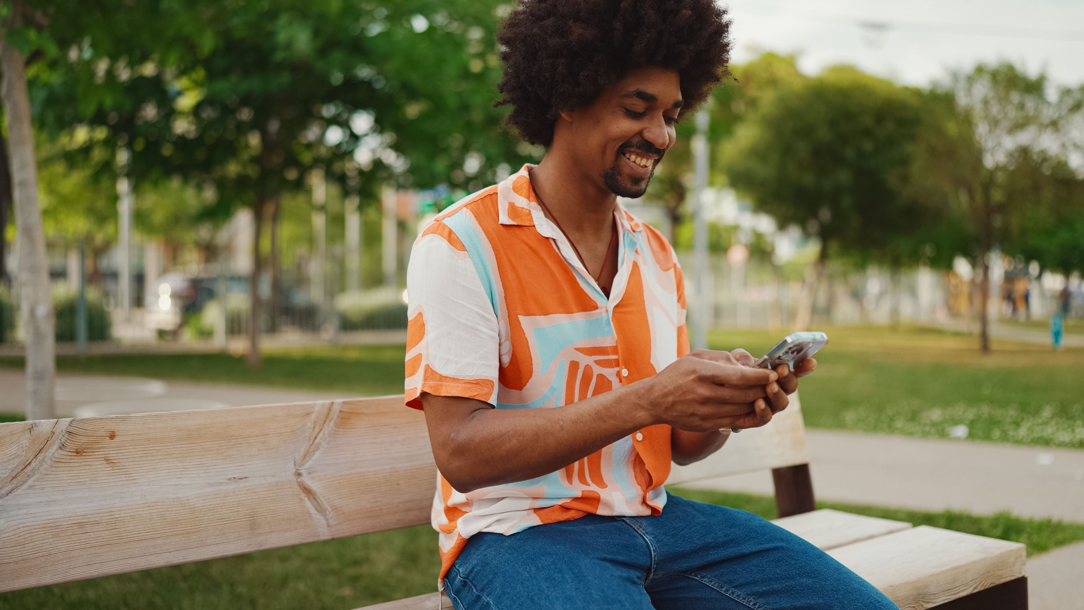 Mann sitzt entspannt auf einer Parkbank und nutzt sein Smartphone – moderner Lifestyle, mobiles Arbeiten und Kommunikation im Freien.