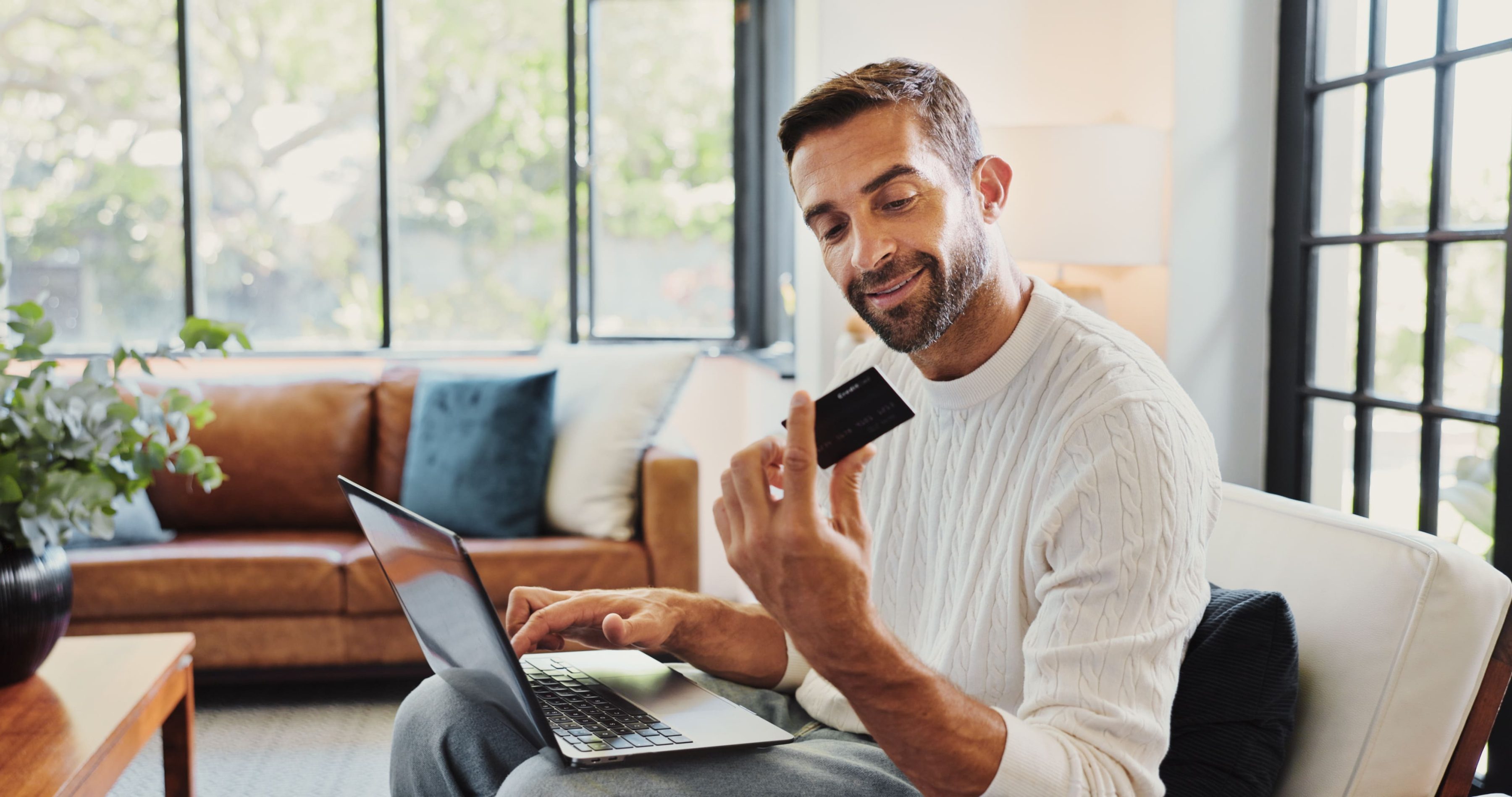 Mann sitzt zu Hause am Laptop und hält eine Kreditkarte – Symbol für sicheres Online-Shopping, digitales Bezahlen und modernen Einkaufskomfort